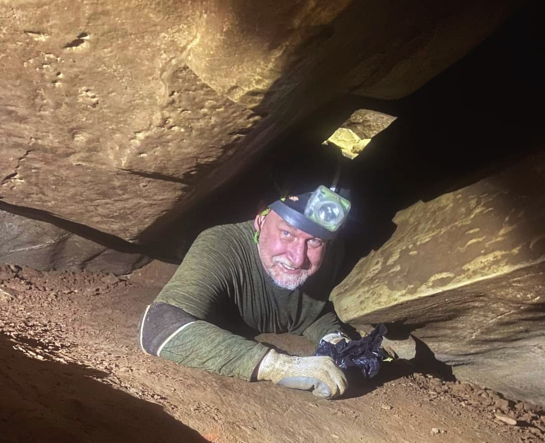 Shawn crawling through a cave passage wearing a headlamp